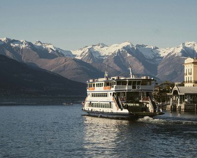 White passenger ferry docked at a pier with snow-capped Patagonian mountains reflected in calm lake waters.