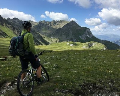 Mountain biker pauses on alpine meadow with dramatic peaks and green valleys in the Swiss Alps.