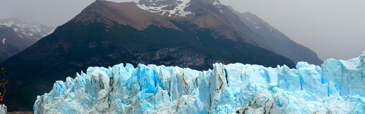 Glaciar Perito Moreno's turquoise ice cliffs tower above milky waters with snow-capped mountain peaks in the background, Patagonia.