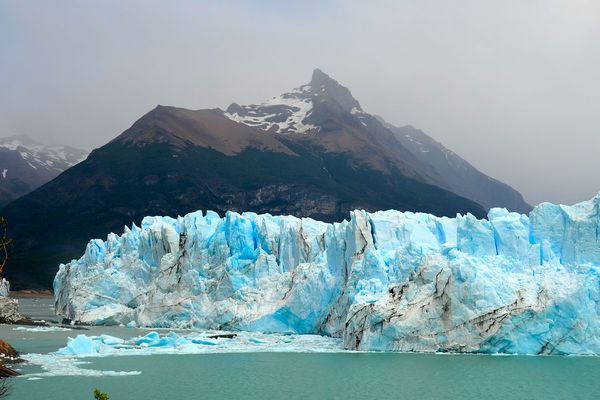 Glaciar Perito Moreno's turquoise ice cliffs tower above milky waters with snow-capped mountain peaks in the background, Patagonia.