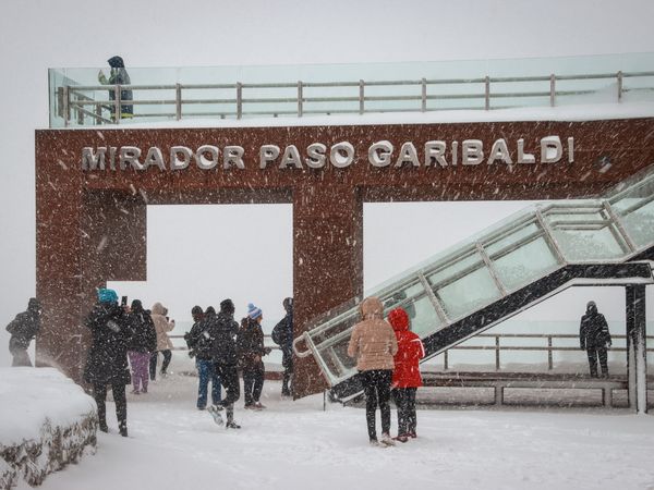 Visitors gather at Mirador Paso Garibaldi viewpoint in heavy snowfall with metal railings and signage visible in Patagonia.
