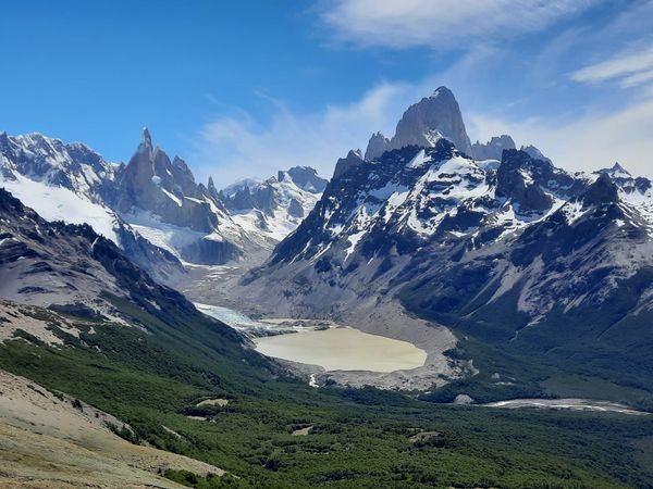Dramatic snow-capped peaks and glaciers surrounding turquoise lagoon in Patagonia's Loma del Pliegue Tumbado mountain landscape.