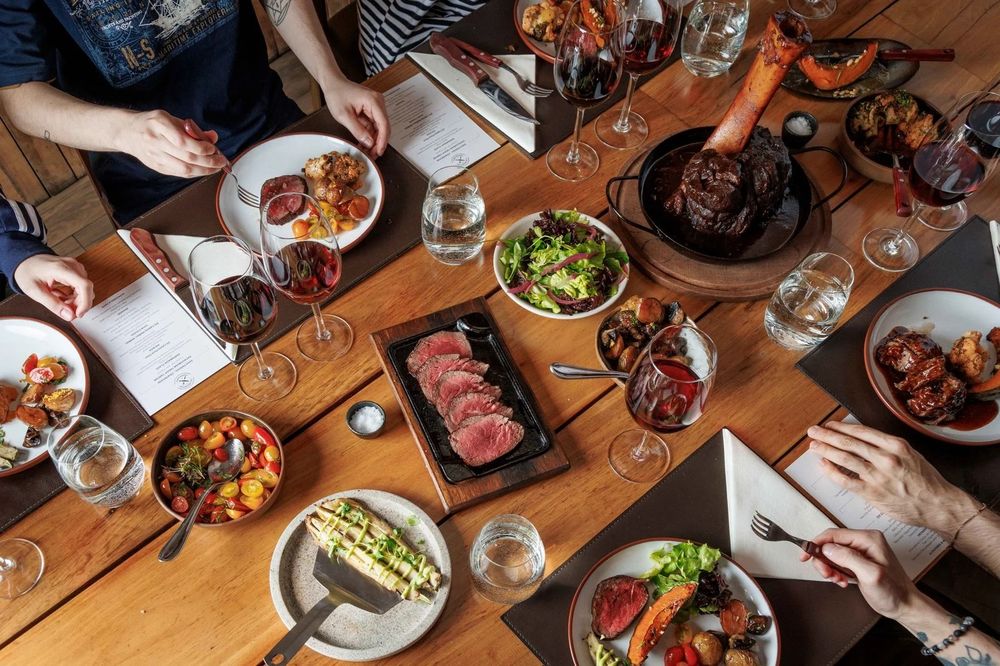 Overhead view of a Buenos Aires dining experience featuring grilled meats, fresh salads, and wine glasses shared among diners at a wooden table.