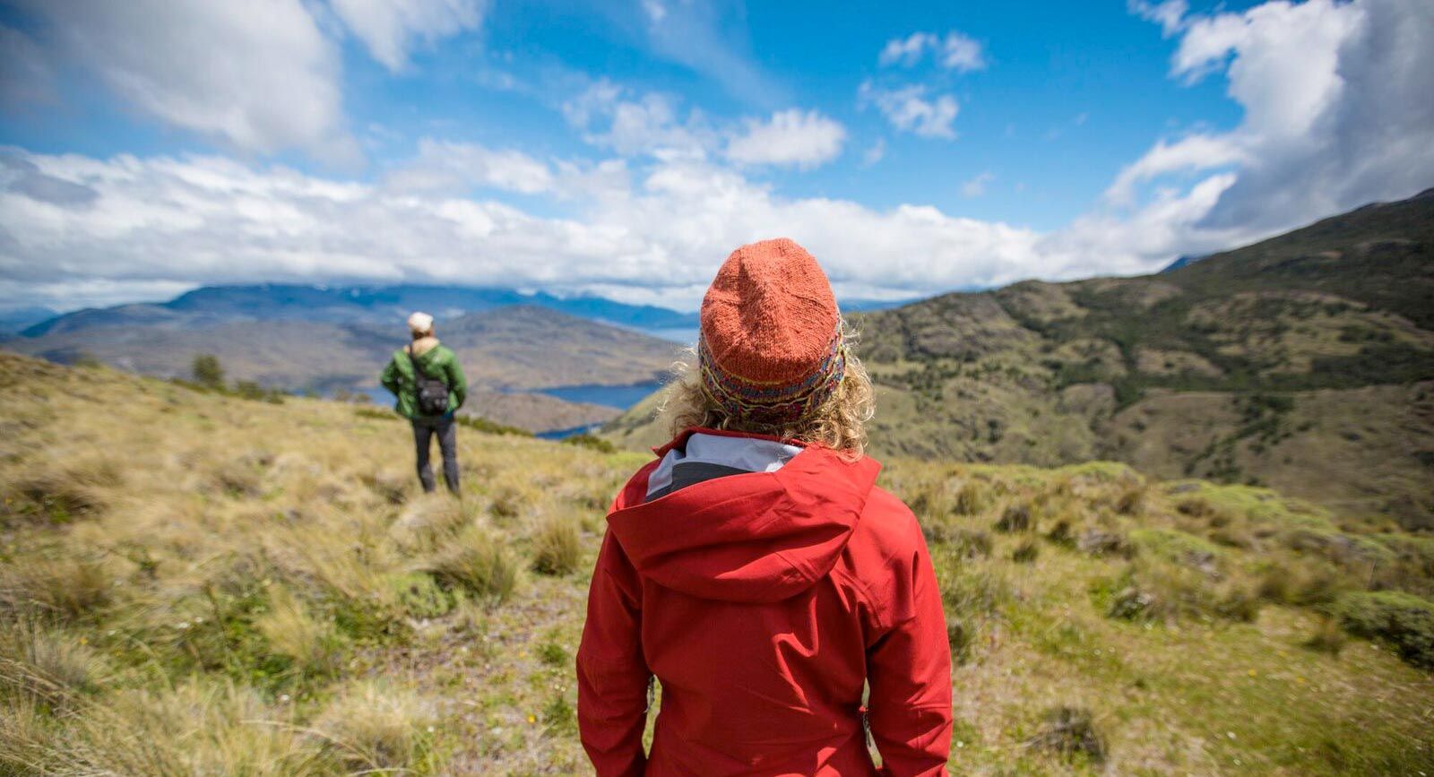 Hikers explore rolling green hills with mountain views in Patagonia, a good fit for an independent self-drive trip