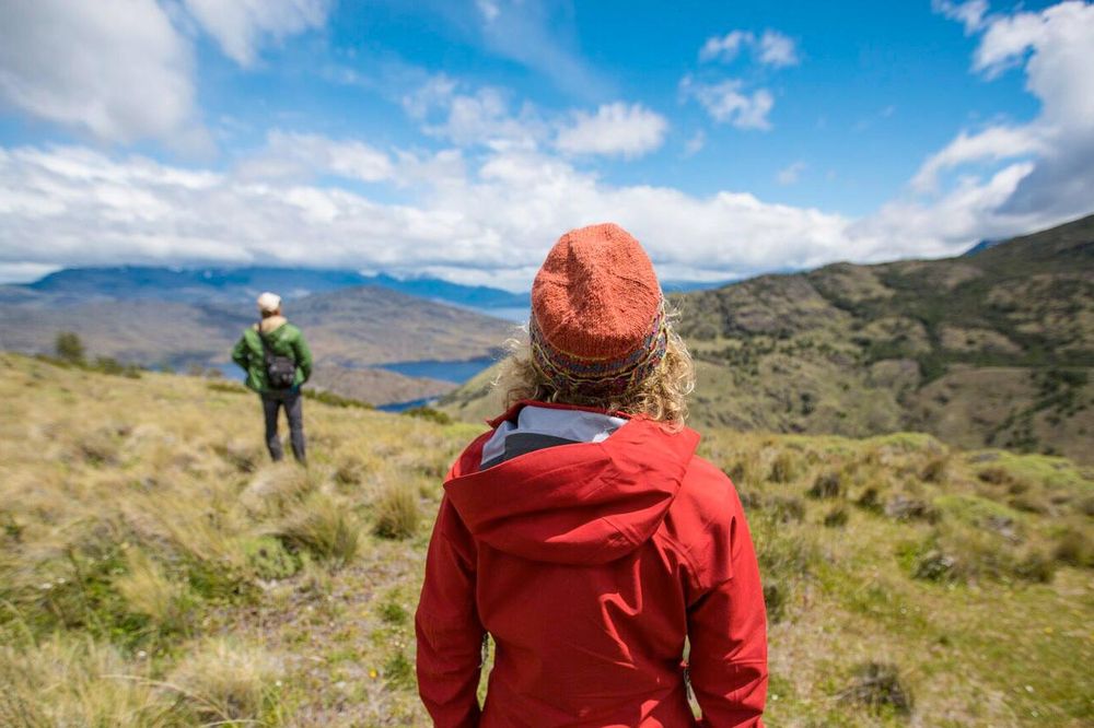 Hikers in red jackets explore rolling green hills with mountain views in Patagonia National Park along the Carretera Austral.