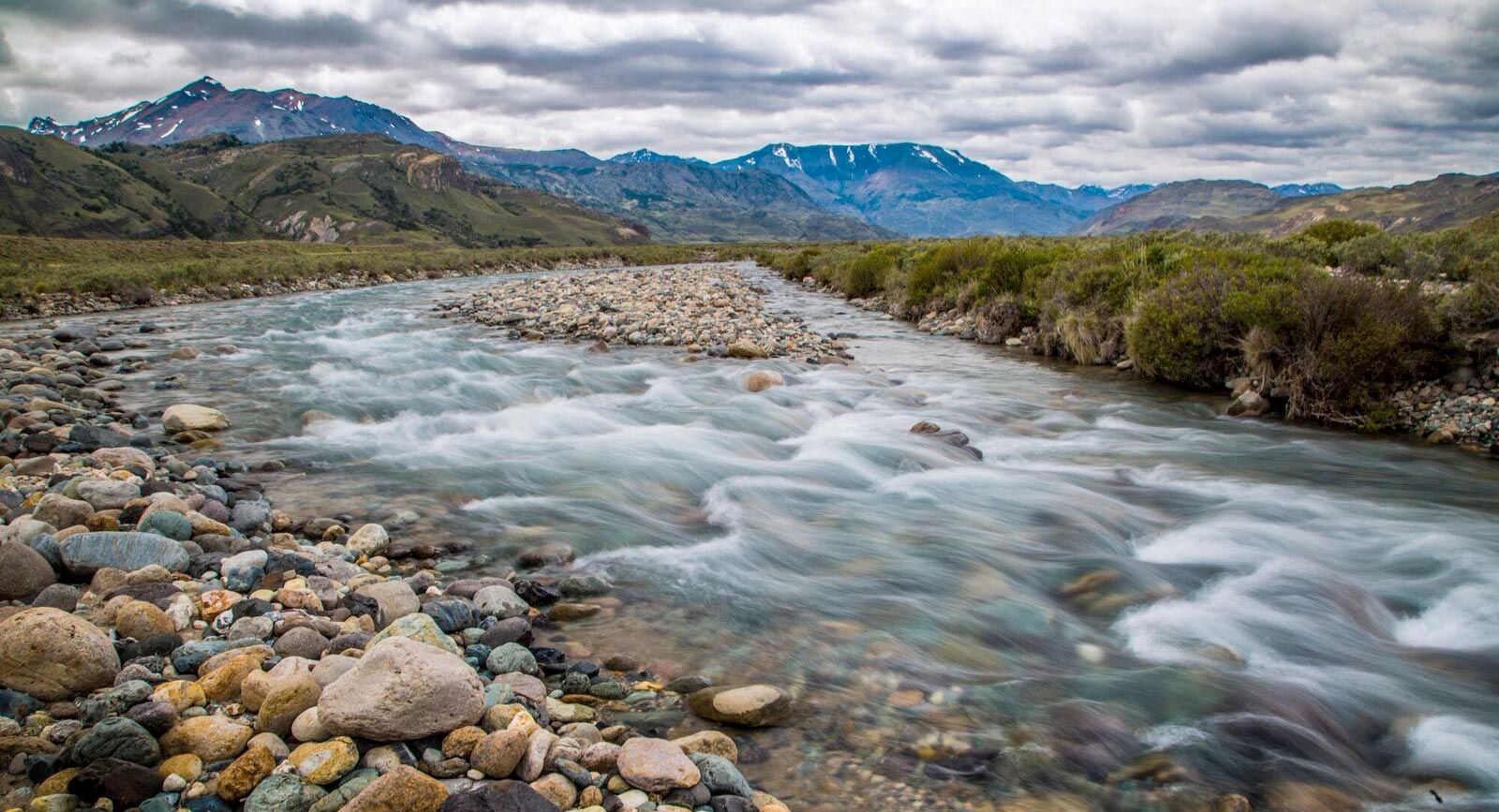 Turquoise river flows through rocky terrain with snow-capped mountains in the Patagonian steppe