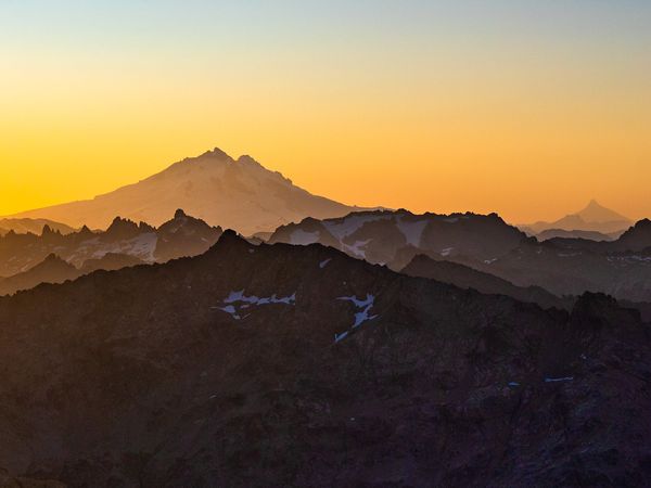 Mount Tronador silhouetted against golden sunrise sky with forested valleys and distant peaks near Bariloche, Patagonia.