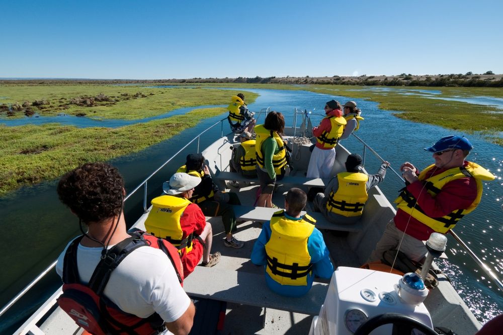 Tourists wearing life jackets navigate Bahía Bustamante's coastal waterway on a guided boat tour through pristine wetlands and tidal rivers.
