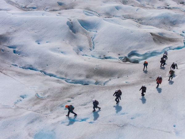 Group of mountaineers trekking across a vast blue and white glacier with dramatic ice formations in Patagonia.