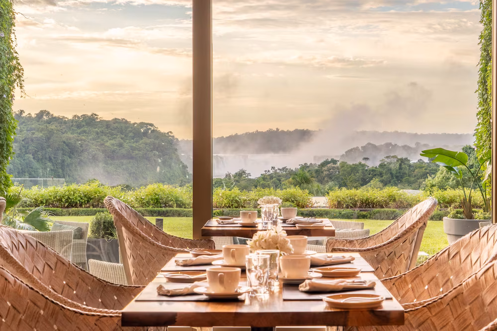 Elegant dining room with woven chairs overlooking Iguazú Falls and misty landscape at Gran Meliá Iguazú.