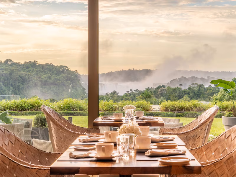 Elegant dining room with woven chairs overlooking Iguazú Falls and misty landscape at Gran Meliá Iguazú.
