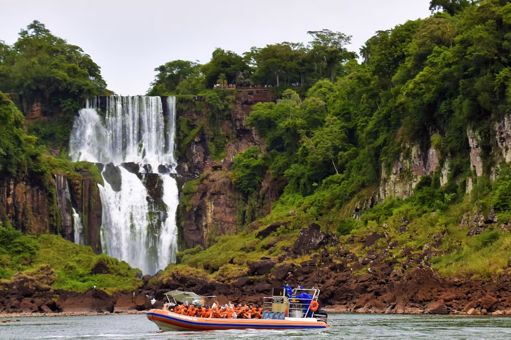 Tourist boat approaches Iguazú Falls with cascading white water and lush green cliffs in Misiones, Argentina.