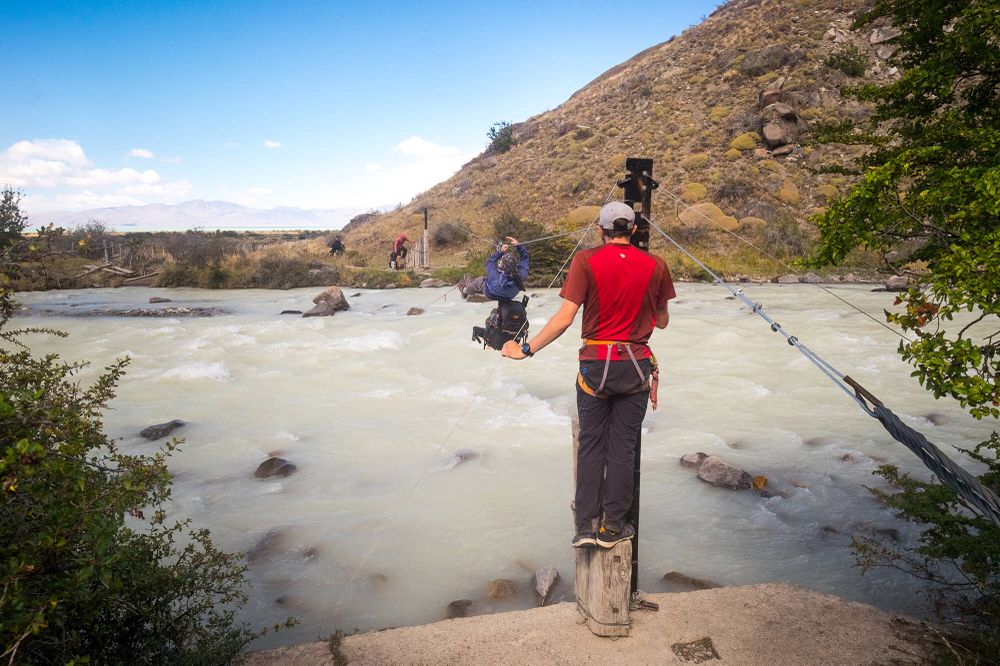 Adventure trekker crosses rope bridge over turquoise glacial river in El Chaltén, Patagonia.