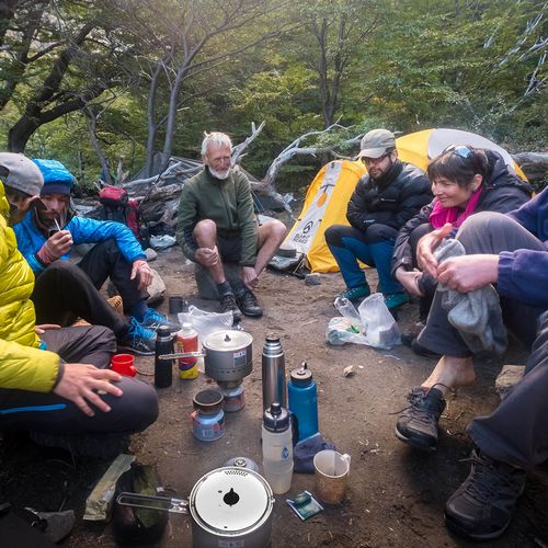 Backpackers gather around a camp stove in a forest clearing during a trek near El Chaltén, Patagonia.