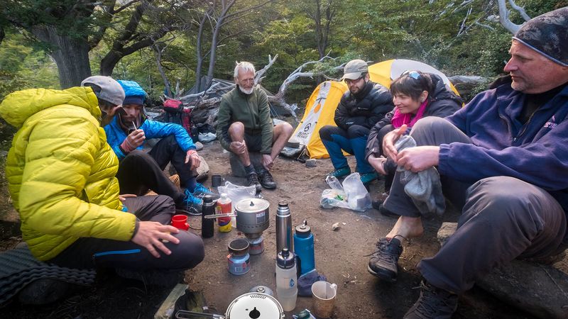 Backpackers gather around a camp stove in a forest clearing during a trek near El Chaltén, Patagonia.