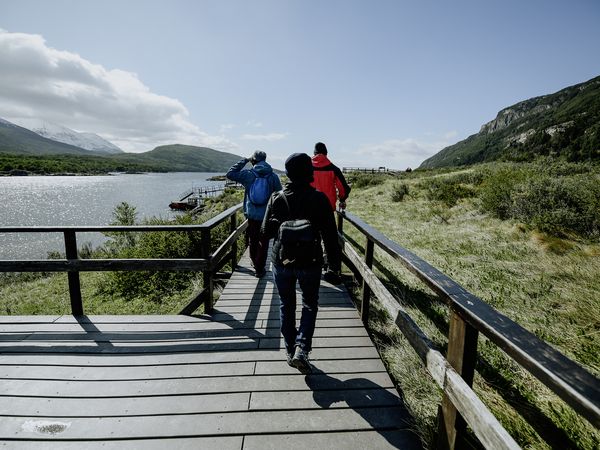 Hikers on wooden boardwalk trail with mountain views at Tierra del Fuego National Park, Patagonia.