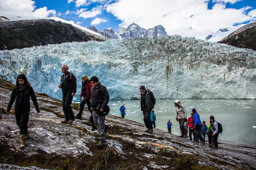Tourists hiking along a glacial lake with turquoise waters and towering blue ice formations in Patagonia.