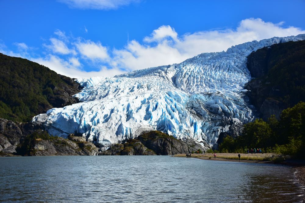 Glaciar Águila cascades down snow-covered peaks above turquoise waters, framed by temperate rainforest in Chilean Patagonia.