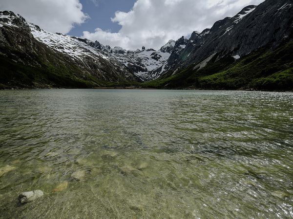 Crystal-clear alpine lake surrounded by snow-capped peaks and lush green valleys in Patagonia's mountain wilderness.