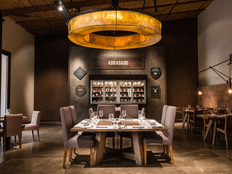 Abrasado restaurant in Mendoza features elegant dining with warm amber lighting, wooden tables, and wine displays on dark walls.