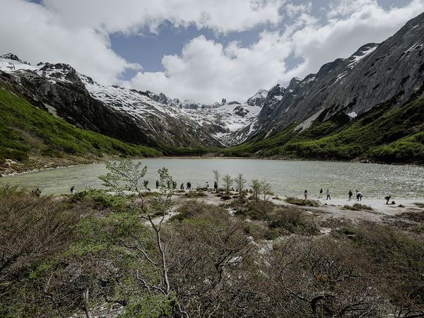 Turquoise glacial lake surrounded by snow-capped peaks and green valleys with hikers wading in Laguna Esmeralda, Patagonia.