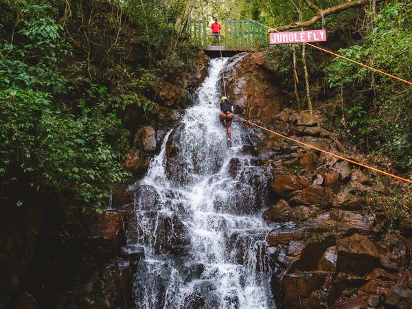 Adventure traveler zip-lining over cascading waterfall in lush Iguazú jungle canopy.