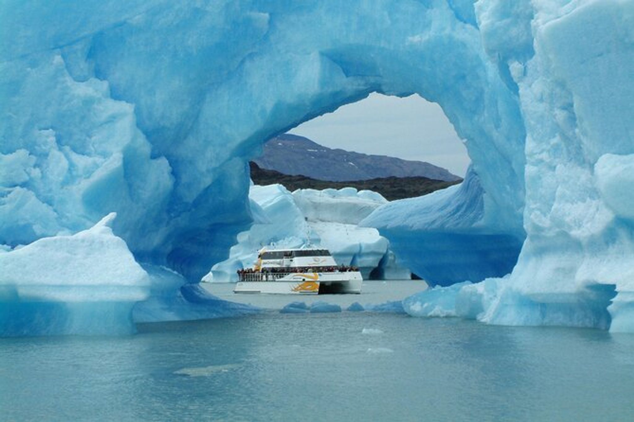 Expedition cruise ship navigates through massive blue ice arches at Glaciar Perito Moreno in El Calafate, Patagonia.