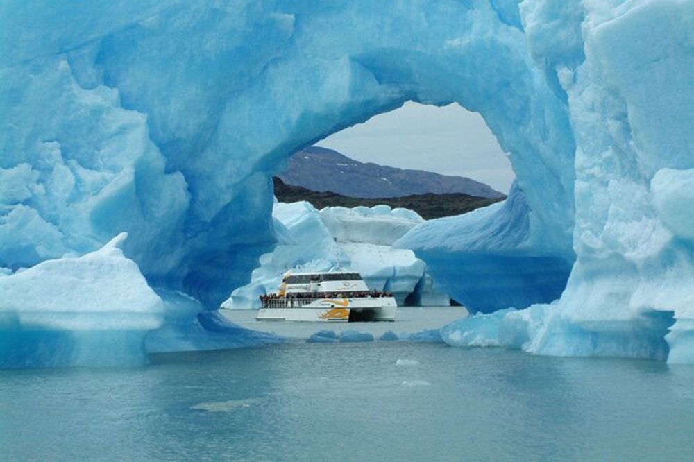 Expedition cruise ship navigates through massive blue ice arches at Glaciar Perito Moreno in El Calafate, Patagonia.