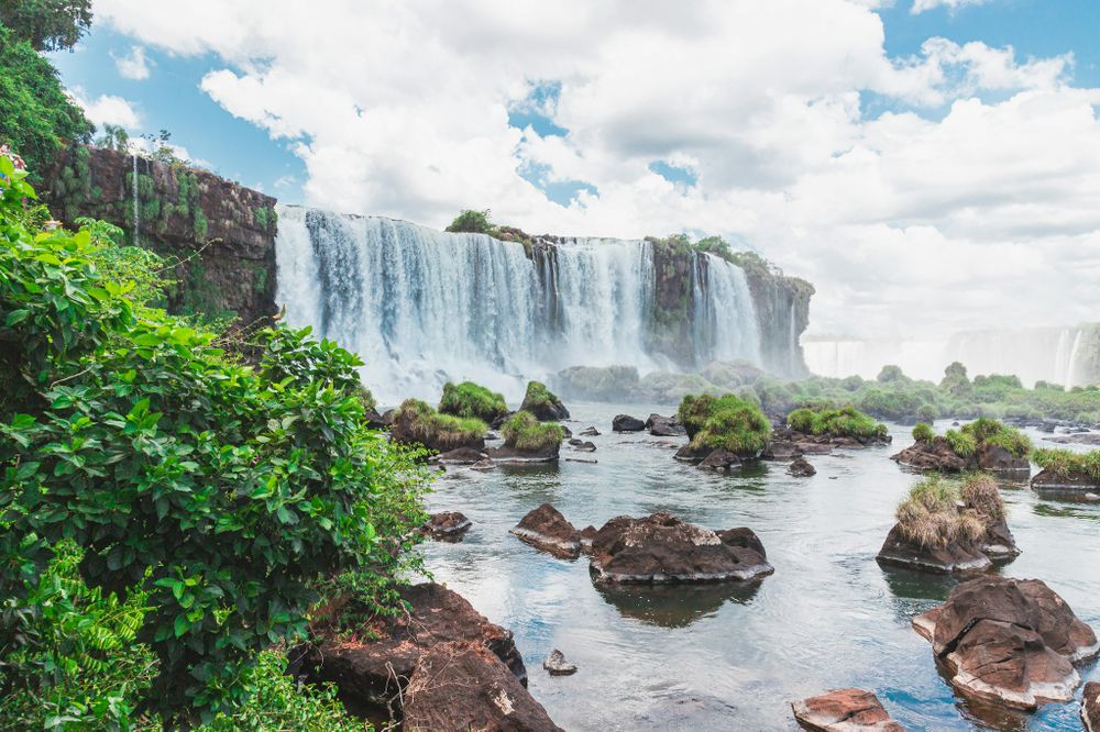 Cascading waterfalls of Iguazú plunge dramatically over basalt cliffs surrounded by lush vegetation and rocky islands.