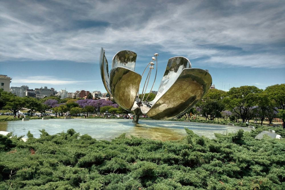 Floralis Generica sculpture blooms beside a pond in Buenos Aires' Parque de la República with jacaranda trees.