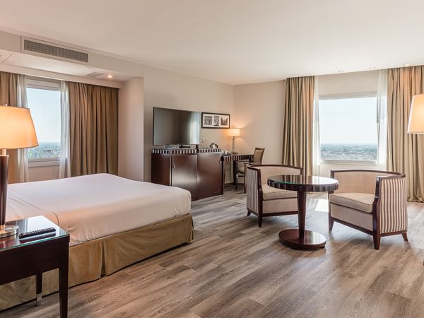 Luxury hotel suite with panoramic city views, modern furnishings, and elegant décor in a high-rise building.