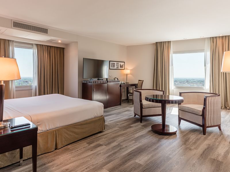 Luxury hotel suite with panoramic city views, modern furnishings, and elegant décor in a high-rise building.