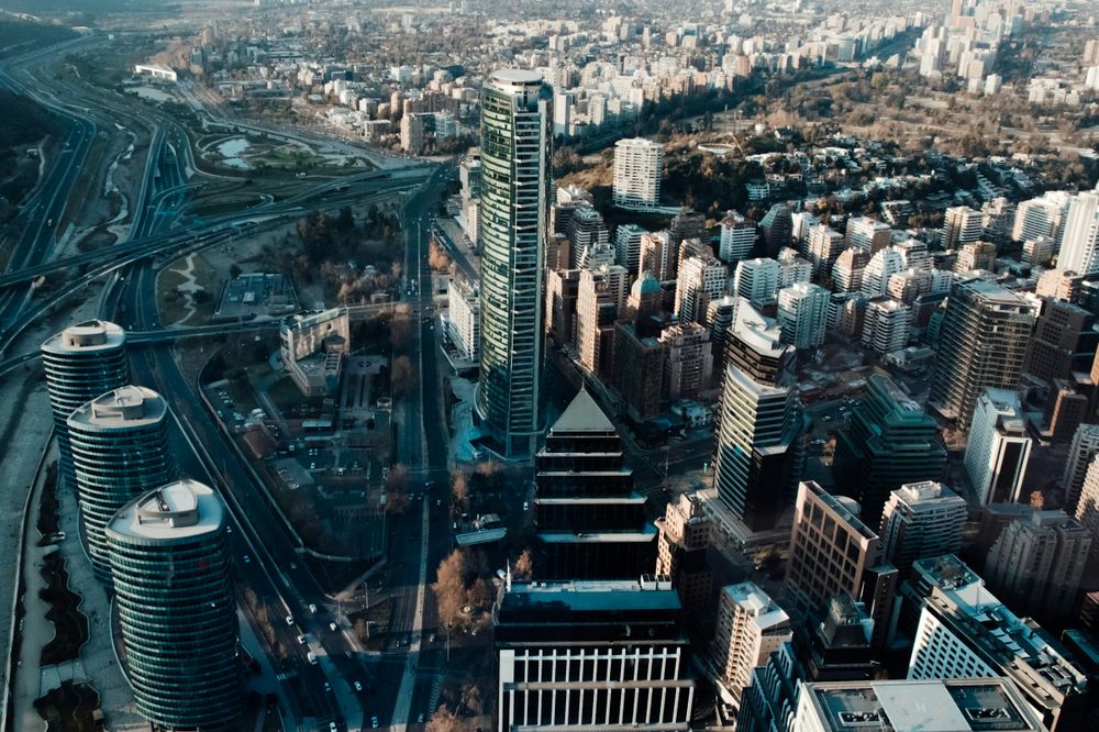 Aerial view of Santiago's downtown skyline with modern skyscrapers, highways, and the Andes Mountains in the distance.