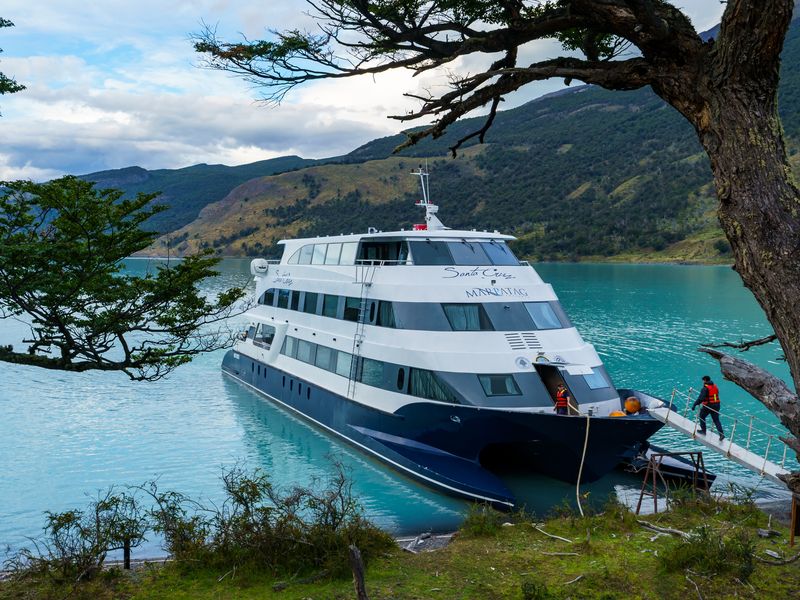 Luxury cruise ship Espíritu de los Glaciares moored in turquoise waters near El Calafate, Patagonia, with snow-capped mountains framing the scenic landscape.