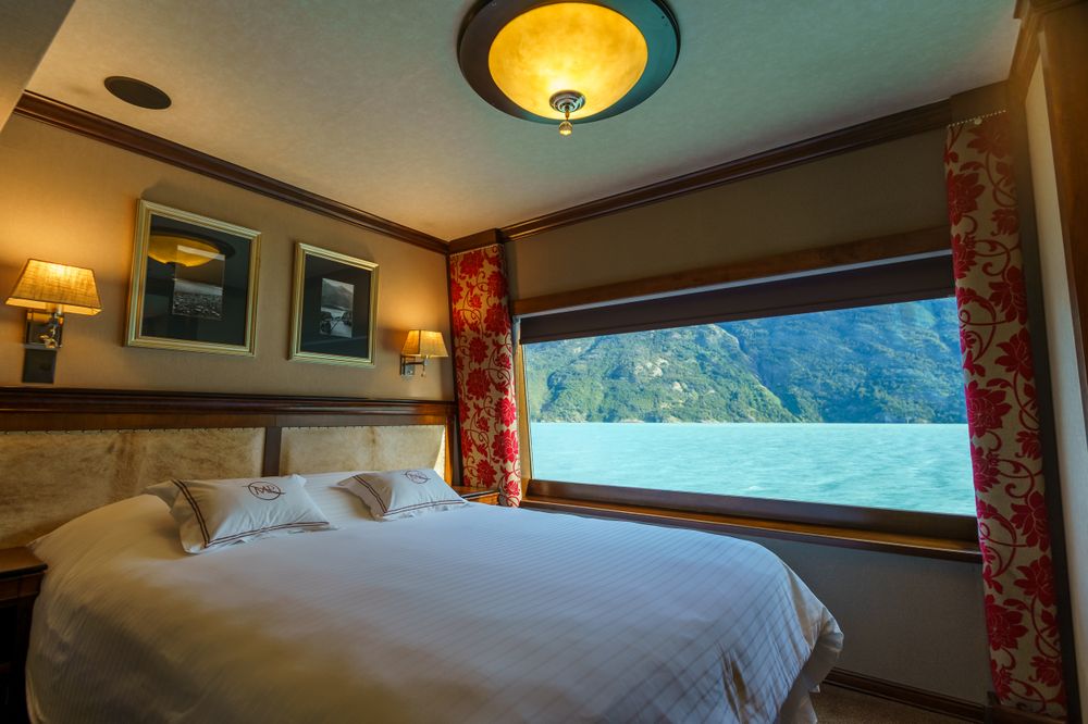 Luxury cruise cabin with panoramic window overlooking turquoise waters and forested mountains near El Calafate, Patagonia.