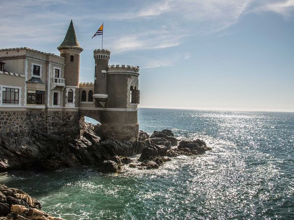 Beachfront castle with towers and Catalan flag overlooking rocky coastline in Viña del Mar, Chile.