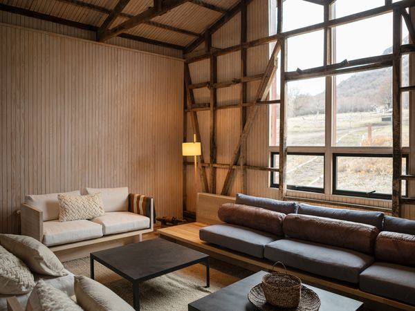 Modern rustic living room with floor-to-ceiling windows overlooking Patagonian countryside and mountains.