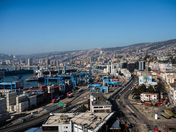 Valparaiso port with blue cargo cranes, hillside neighborhoods, and Pacific Ocean under clear sky.