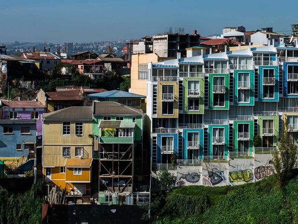 Colorful stilt houses and buildings overlook a green ravine in the vibrant hillside neighborhood of Valparaíso, Chile.