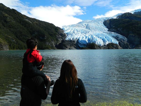 Family viewing a massive blue glacier across turquoise waters in the Cruce Andino region near Puerto Varas, Patagonia.
