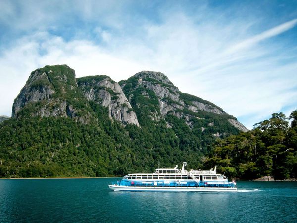 Cruce Andino ferry boat navigates turquoise waters with dramatic forested mountains and rocky peaks in Patagonia.