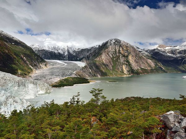 Glacier-fed turquoise lake surrounded by snow-capped peaks and verdant forests along the Cruce Andino route near Puerto Varas.