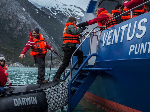 Passengers board the Ventus Australis boat from a zodiac in a snow-capped Patagonian fjord during the Cruce Andino crossing.