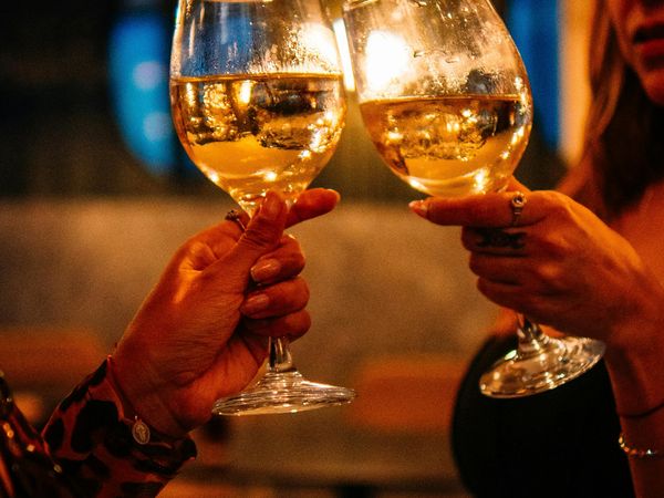 Two people clink wine glasses during an evening celebration in Buenos Aires, toasting with golden wine under warm lighting.