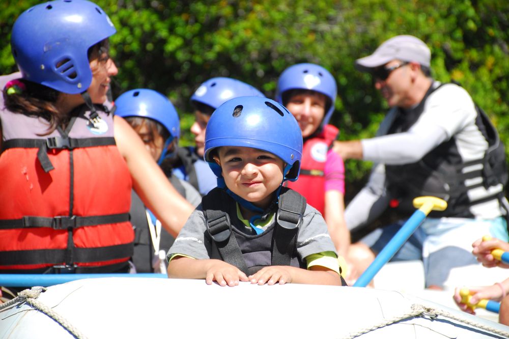 Children in safety helmets and life jackets enjoy a family whitewater rafting adventure on a river near Bariloche.