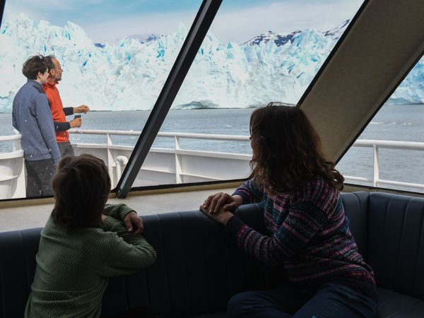 Tourists viewing Perito Moreno Glacier from inside a tour boat's enclosed cabin in Patagonia, Argentina.