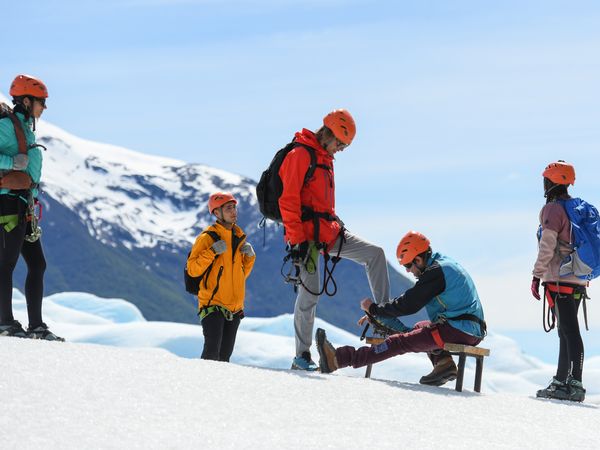 Group of climbers in safety gear rest on snowy glacier with snow-capped Patagonian mountains in background.