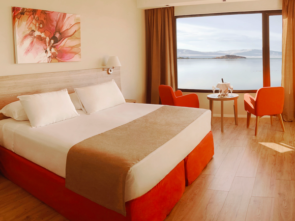 Modern hotel bedroom with red accents overlooking a Patagonian lake and mountains through floor-to-ceiling windows.