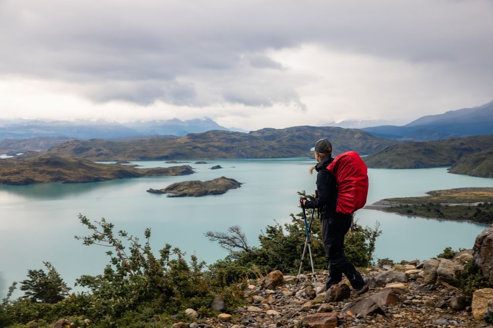 Hiker with trekking poles overlooking turquoise lakes and mountains at Valle Francés in Torres del Paine, Patagonia.