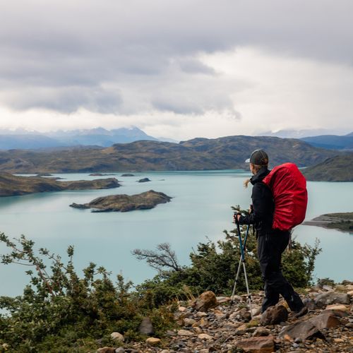 Hiker with trekking poles overlooking turquoise lakes and mountains at Valle Francés in Torres del Paine, Patagonia.